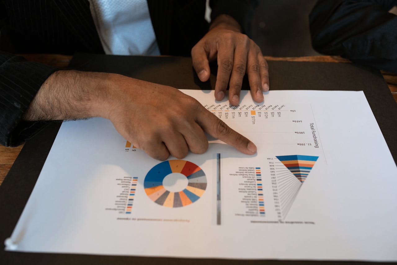 Hands pointing at colorful graphs and charts in a workspace. Ideal for business presentations and reports.